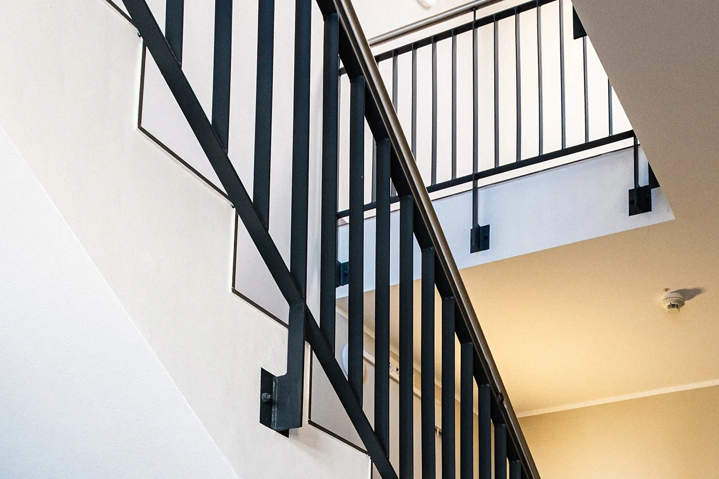 Moderne Treppenanlage mit pulverbeschichtetem schwarzen Metallgeländer und sauber verputzten, hellen Wänden – hochwertiger Innenausbau im Treppenhaus.